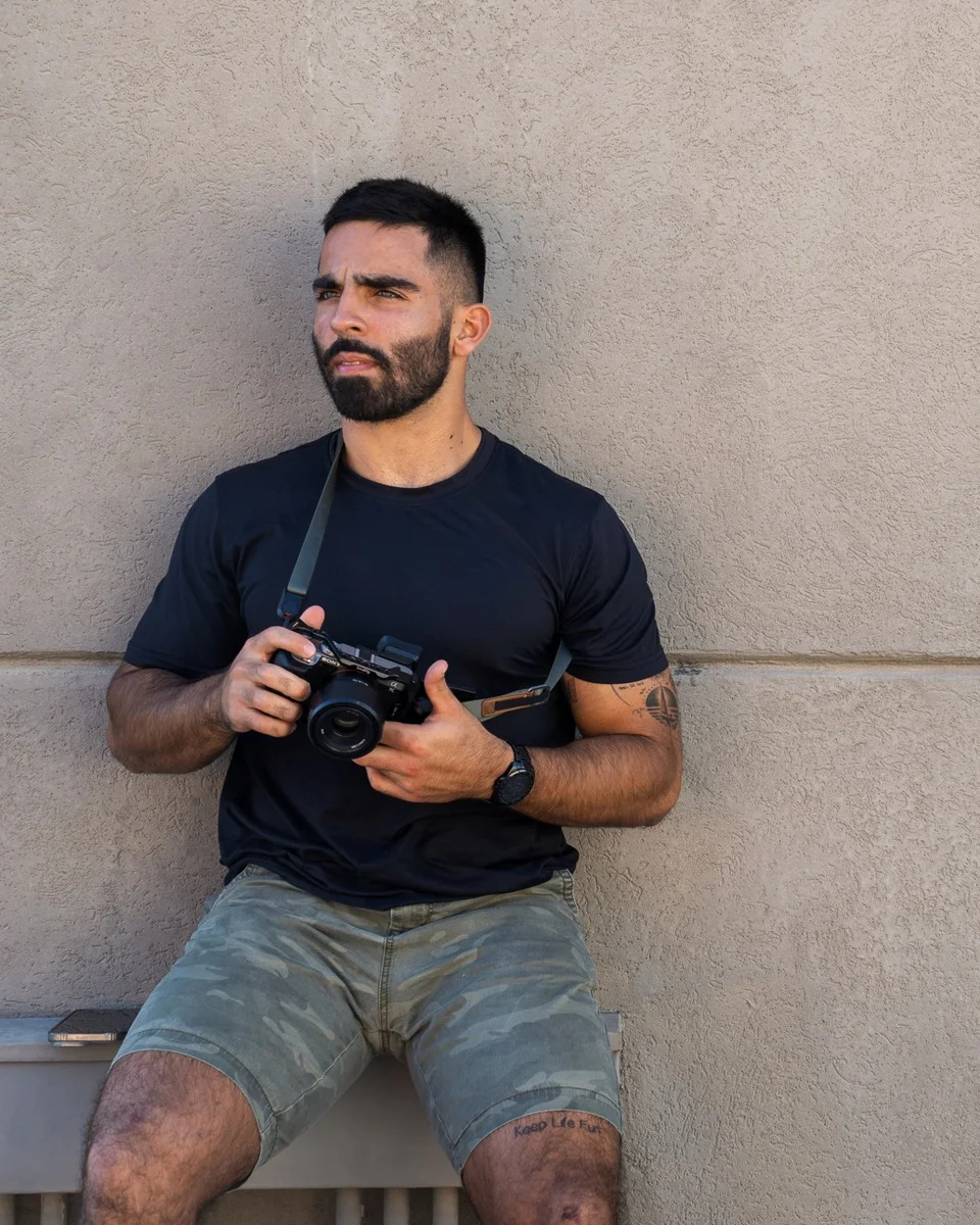 Ivan Sanchez sitting against a wall holding his camera