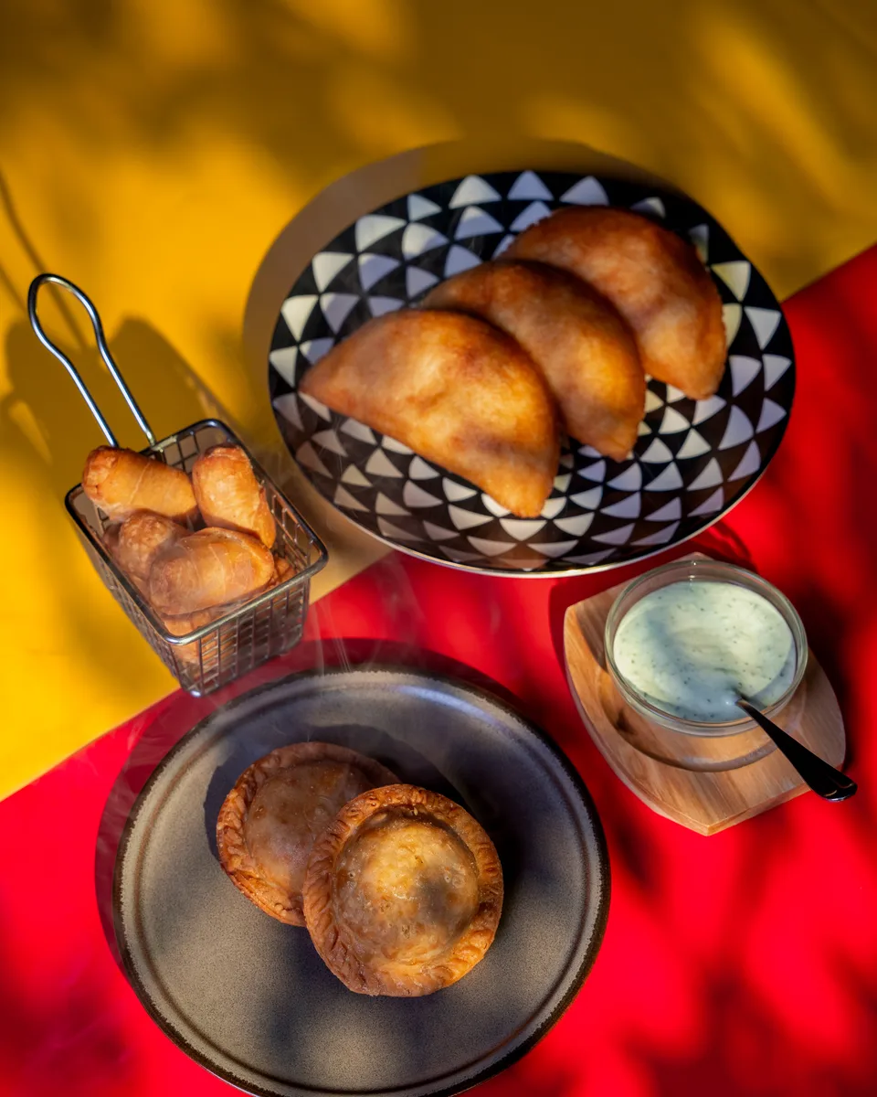 Golden empanadas with green sauce on a yellow and red table